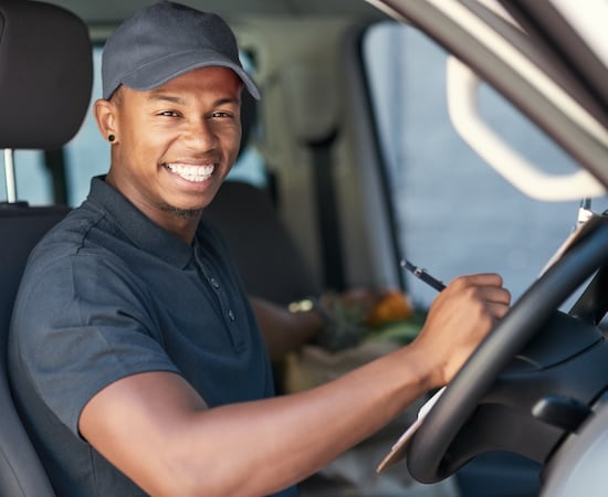 Smiling delivery driver holding a clipboard behind the wheel of a fleet vehicle