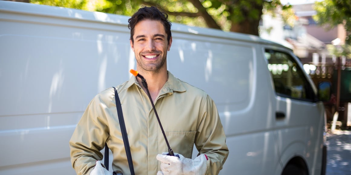 Smiling pest control worker in front of van after learning what fleet management is
