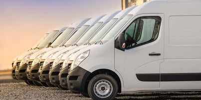 Row of white delivery vans equipped with a fleet management system parked in a lot at sundown